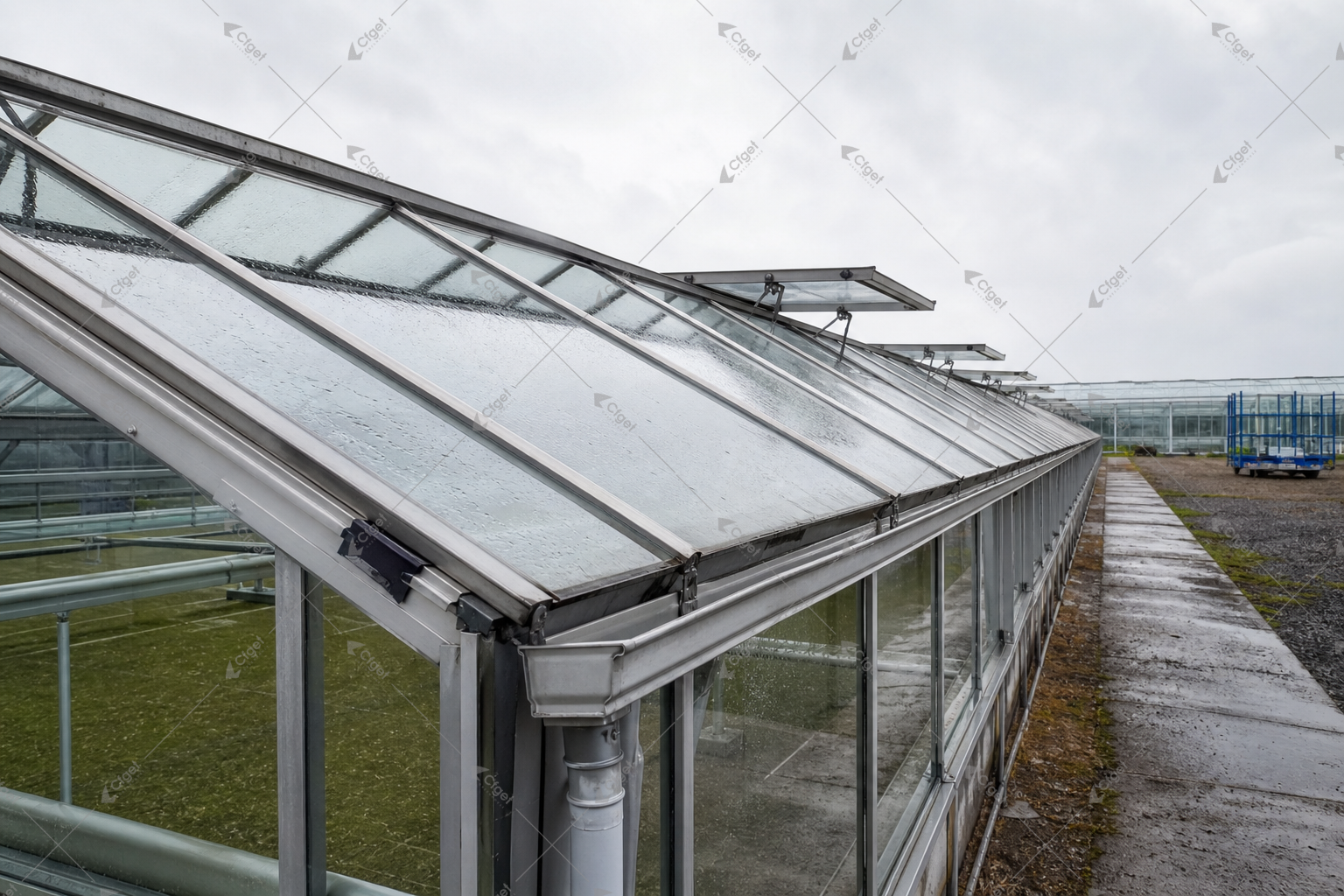 Cleaning limits, drainage, safe roof access, and future pane supply belong in the ownership-cost comparison. working glass greenhouse roof and gutters after rain with realistic maintenance access